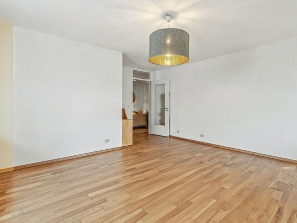 Helles Zimmer mit Holzboden, Deckenleuchte und Zugang zum Flur