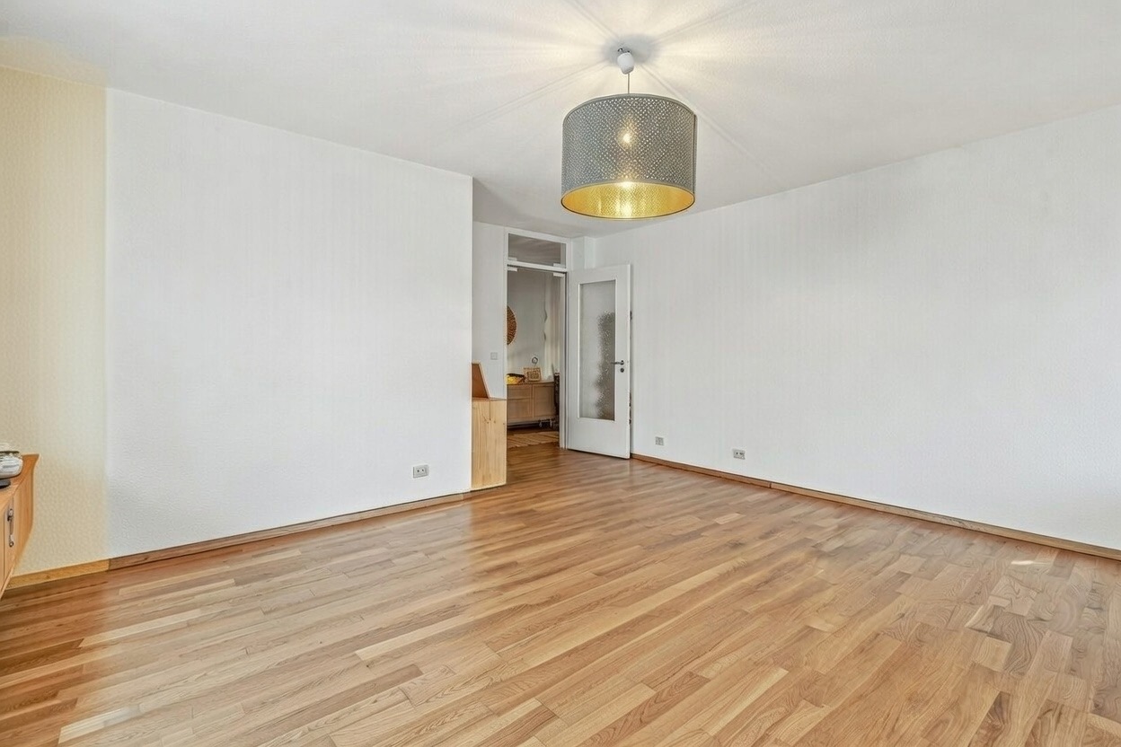 Helles Zimmer mit Holzboden, Deckenleuchte und Zugang zum Flur